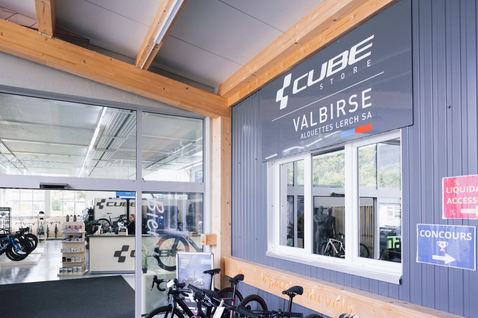 Eingang des CUBE Store Valbirse mit dem Wegweiser zum Gewinnspiel